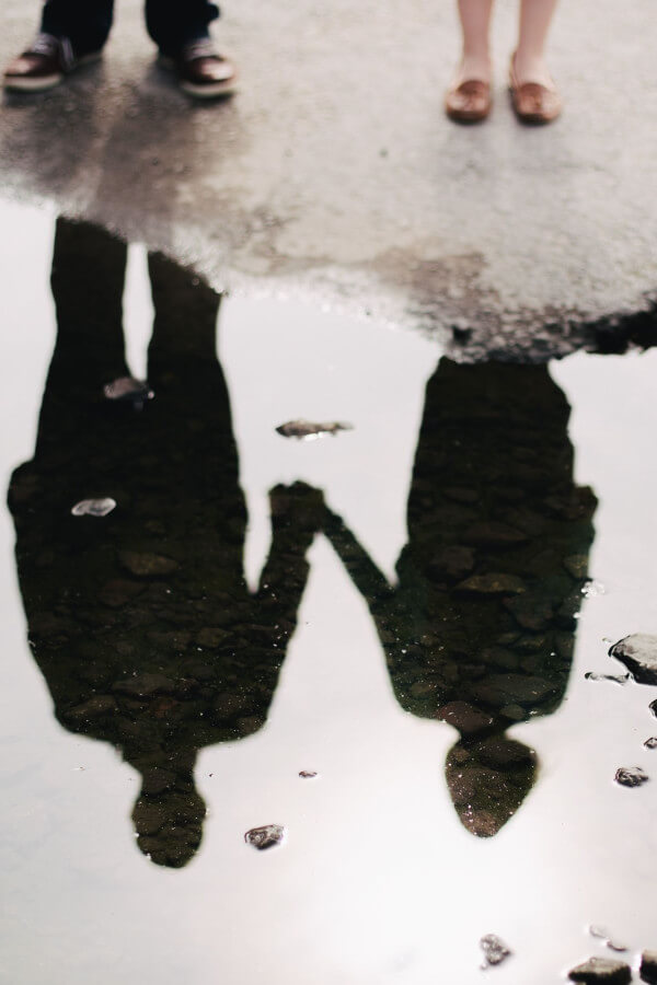 A Couple standing next to a puddle of water looking at their reflection in the water.